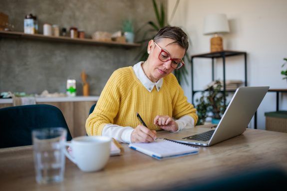 Stylish entrepreneur wearing eyeglasses working on computer at home. Woman analyzing and managing domestic bills and home finance